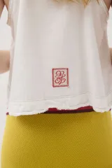 Top de jean blanco sin mangas, con escote redondo, espalda deportiva, costuras pespunteadas en el frente y ruedo desmechado.