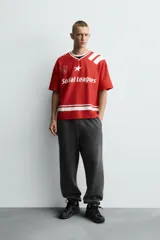 Camiseta de manga corta color rojo, corte boxy fit, con cuello pico ribeteado en blanco. Presenta un estampado frontal con el texto "Social Leagues", una estrella blanca y un escudo con el número "4". Tiene detalles de franjas blancas en el bajo y en los hombros.