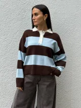 Sweater tipo chomba de tejido bremer con diseño de rayas horizontales en color marrón y celeste. Presenta cuello polo en color crema con cierre frontal de botones y mangas largas.