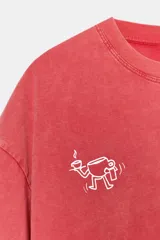 Remera de corte oversize con efecto lavado, color rojo, cuello redondo y manga corta con hombro caído. Presenta un estampado pequeño en el pecho con el logo de la marca y un dibujo lineal de una taza de café.