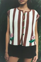 Chaleco tejido a rayas verticales en color marrón y celeste, con botones frontales y un bordado artesanal de una flor en la parte inferior.