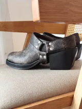 Zueco de cuero con efecto desgastado en tono visón, con diseño de punta cuadrada, suela gruesa negra y detalle de correa con tachas metálicas y argolla lateral.