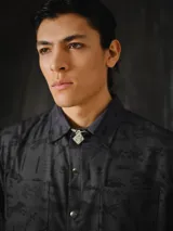Camisa de manga corta color gris oscuro con estampa exclusiva de símbolos, animales y elementos de la marca en tono negro. Presenta cuello camisero, dos bolsillos delanteros con solapa, corte relajado y cierre frontal con botones metálicos a presión.