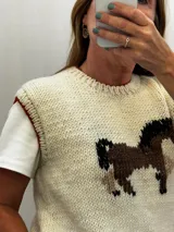 Chaleco tejido de punto color marfil, confeccionado en 100% lana merino, con cuello redondo y diseño frontal bordado artesanalmente que representa un caballo en tonos marrones y negros.