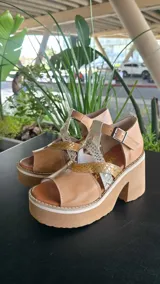 Sandalias de cuero color suela, con plataforma alta y taco ancho. Diseño con tiras cruzadas y apliques en texturas metalizadas y animal print, cierre con hebilla en el tobillo.