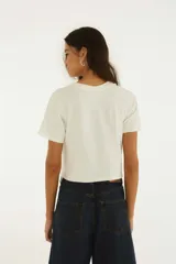 Remera blanca de manga corta y cuello redondo, confeccionada en algodón, con estampado frontal de dos tulipanes rojos y detalles de lazos de satén en el dobladillo.