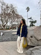 Cartera tipo hobo de cuero gamuzado color verde oliva, con cierre superior y correa ajustable. Presenta una etiqueta de cuero con el logo de la marca en el frente.