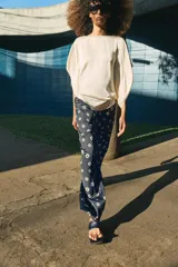 Pantalón de tiro medio con cintura elástica y bolsillos ocultos en costura. Presenta un diseño de corte recto con dobladillo ancho en el bajo y un estampado geométrico sobre fondo oscuro.