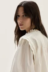 Blusa blanca de algodón con escote alto, detalles de smock y tablitas en el canesú y hombros, y mangas largas abullonadas con puños fruncidos.