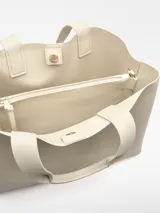 Bolso shopper horizontal de poliuretano color beige, con dos compartimentos, cierre magnético, bolsillo interior con cierre, asa de mano y asa larga regulable y extraíble. Incluye logo grabado en el frente.