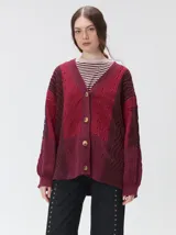 Cardigan oversize de tejido de punto grueso con diseño de bloques de color en tonos beige y marrón. Presenta cuello en V, cierre frontal con botones, mangas largas abullonadas y parches decorativos en el pecho y el hombro.