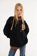 Sweater de punto oversize con diseño estilo universitario vintage, color negro con detalles en marrón en el cuello y el ruedo. Presenta una letra bordada en el frente en color blanco y marrón.