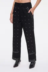 Pantalón negro de corte carrot, con bolsillos laterales, cierre frontal y aplicación de tachas metálicas en toda la prenda y en los dobladillos.