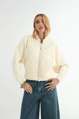 Abrigo tipo bomber de color crema, con frente acolchado en diseño de rombos y mangas tejidas en punto acanalado. Presenta cierre frontal completo y cuello redondo.