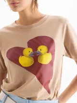 Remera gris oscuro con efecto acid wash, corte clásico, mangas cortas y cuello redondo. Cuenta con una estampa frontal de un corazón rojo con dos patitos amarillos besándose.