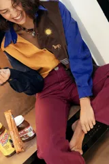 Camisa amplia de pana con diseño en bloques de color azul, amarillo y marrón, con cuello clásico, mangas largas y bordados decorativos de sol, caballo y bandera en el frente.
