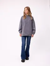 Canguro oversize de color gris con efecto lavado, capucha con cordones ajustables, bolsillo frontal tipo canguro y parche pequeño con logo de la marca en el pecho.