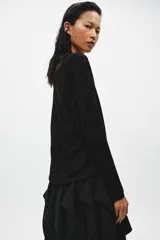 Jersey de punto fino negro con escote en V pronunciado, mangas largas y corte holgado con bajo asimétrico, más largo en la parte trasera.