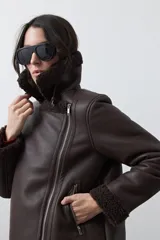 Campera tipo gamulán de símil cuero color marrón oscuro, con interior y solapas de corderito al tono. Presenta cierre frontal cruzado, bolsillos con cierre metálico y hebilla ajustable en el cuello.