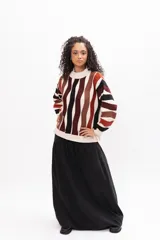 Buzo de tejido de punto con diseño de rayas verticales onduladas en tonos tierra, negro y crema. Presenta cuello redondo, mangas largas y corte holgado.