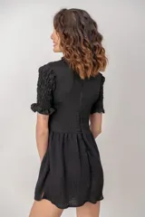Vestido corto de color negro, con cuerpo y mangas cortas de nido de abeja fruncido, y falda corta con vuelo.