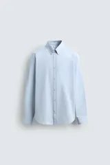Camisa de corte slim fit confeccionada en tejido de algodón, color celeste. Cuenta con cuello abotonado, manga larga con puños ajustables mediante botón y cierre frontal con botonadura.