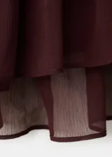 Blusa fluida color bordó, con escote en V, mangas largas con volantes en los puños y detalles de volantes en el frente y el cuello.