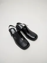 Zuecos de cuero vacuno con acabado en charol, color beige. Presentan un diseño clásico con taco cuadrado de madera de 5 cm y correa trasera ajustable con hebilla metálica.