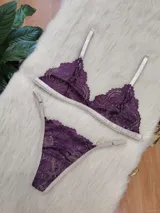 Conjunto de lencería compuesto por un bralette triangular y una bombacha tipo tanga, confeccionados en encaje color violeta con terminaciones y breteles en color tostado.