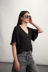 Camisa negra con botones dorados, escote en V y mangas cortas amplias con lazos laterales. 