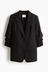 Blazer largo color negro con solapas de muesca, cierre de un botón, bolsillos delanteros ribeteados, hombreras y mangas tres cuartos fruncidas.