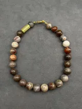 Collar de piedras naturales en tonos tierra, con detalle de tubo dorado en un lateral y cierre marinero dorado.