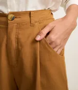 Bermuda color ocre de sarga, con cintura alta elástica, cierre con botón y cremallera, bolsillos laterales y pliegues delanteros.