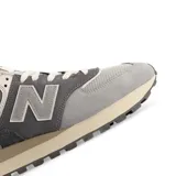 Championes urbanos New Balance modelo 574, con diseño en tonos grises y detalles en marrón. Confeccionados en una combinación de gamuza y malla, cuentan con el logo lateral característico y entresuela con tecnología ENCAP para mayor amortiguación.