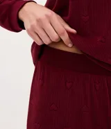 Pijama de dos piezas confeccionado en plush con textura acanalada y estampado de corazones en relieve. Incluye una blusa de cuello redondo con mangas largas y puños ajustados, y un pantalón con cintura elástica y puños en el ruedo.