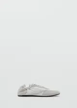 Sneaker Sofi de estilo minimalista en color gris claro, confeccionada en una combinación de piel vacuna y poliéster con detalles de gamuza en la puntera y el talón. Presenta cierre con cordones y un diseño fruncido en la parte trasera con elástico.