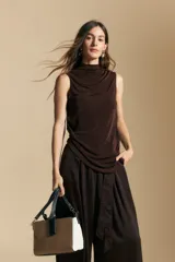 Top sin mangas de color negro con cuello alto y diseño drapeado en el frente. Confeccionado en una tela suave con acabado levemente satinado y silueta fluida.