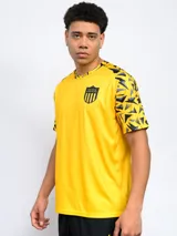 Remera deportiva de hombre, color negro, con cuello redondo y mangas cortas con estampado geométrico en amarillo y gris. Lleva el escudo de Peñarol en el pecho.