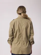 Campera color beige, estilo cazadora, con cuello camisero, cierre frontal con botones, cuatro bolsillos frontales con solapa y mangas 3/4 con trabillas.