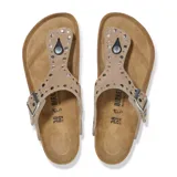 Sandalias tipo ojota Birkenstock modelo Gizeh Rivet en color taupe. Presentan una tira superior de gamuza con tachas metálicas decorativas, hebilla ajustable lateral y plantilla anatómica de corcho con suela de goma negra.