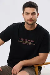 Remera negra de algodón de manga corta con cuello redondo y letras bordadas en el pecho con las frases "Legacy Brand", "Original T.M Since Nineteen Seventy-Two" y "Southampton, NY".