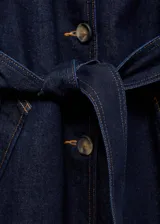 Abrigo largo de denim color azul oscuro, con cuello de solapa, cierre frontal de botones y cinturón ajustable tipo batín. Presenta diseño recto, manga larga y dos bolsillos laterales.