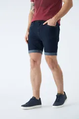 Bermuda de jean azul oscuro con diseño de cinco bolsillos, cierre de cremallera y botón, y detalle de botamanga doblada.
