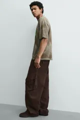 Pantalón cargo de corte relajado confeccionado en tejido de algodón con efecto lavado. Presenta cintura con pliegues frontales, bolsillos laterales con solapa en las perneras, bolsillos frontales y bolsillos traseros con solapa. Cierre frontal con cremallera y botón.