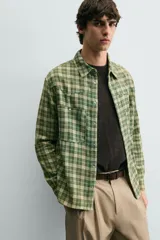 Camisa de corte relajado confeccionada en tejido de algodón con estampado de cuadros en tonos verdes y beige. Presenta cuello solapa, cierre frontal con botones a presión, bolsillos plastrón en el pecho y mangas largas con puños abotonados.