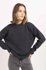 Buzo de punto en color gris oscuro, con cuello redondo acanalado, mangas largas con puños ajustados y diseño de corte holgado.