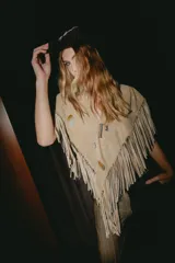 Chall de gamuza natural con diseño triangular, decorado con pins metálicos y flecos largos en todo el borde inferior, estilo western.