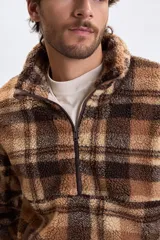 Buzo de sherpa con diseño a cuadros en tonos marrones y beige, cuello alto con medio cierre frontal y bolsillos laterales.