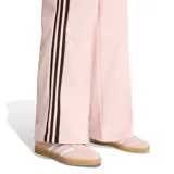 Pantalón deportivo Adidas de corte holgado y pernera ancha, en color rosado con bandas laterales oscuras y el clásico logo del trébol bordado. Cuenta con cintura elástica y bolsillos laterales.