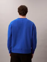 Buzo de felpa azul con cuello redondo, manga larga y corte regular. Presenta puños y dobladillo acanalados, con el logo y bordado 'Very' de Calvin Klein en el pecho.